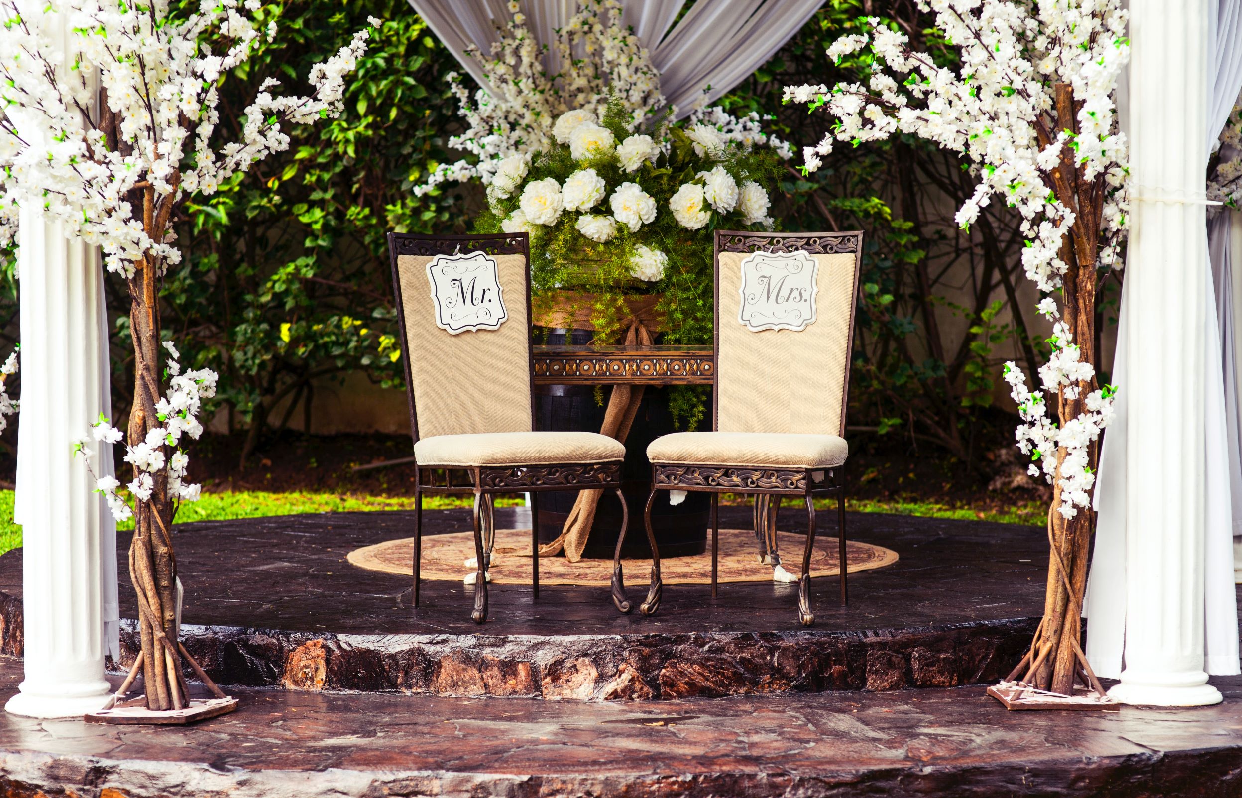 Promising Signs: Image of two chairs under a wedding gazebo with "Mr" and "Mrs" signs on them. The Gazebo has white drapes and flowers