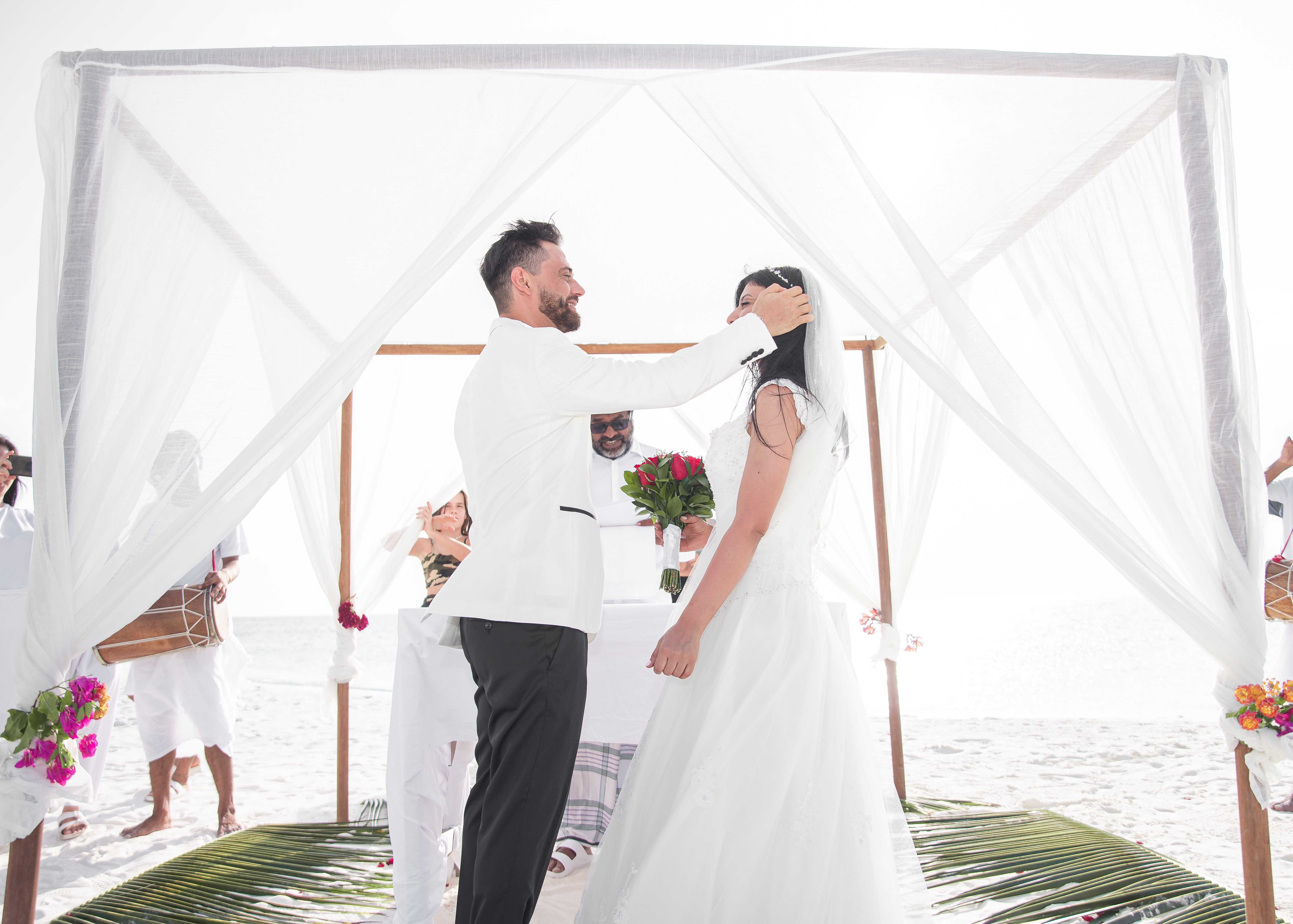 Promising Signs Image shows a couple under a beach canopy with a celebrant. The groom is pushing back the bride's hair